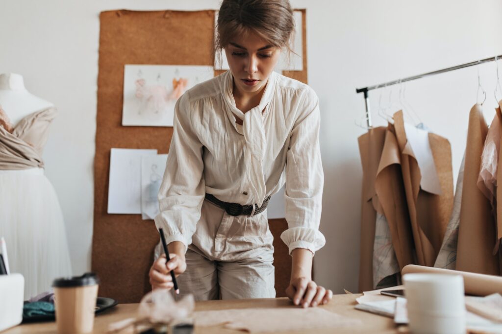 Charming woman in beige outfit making outfit patterns. Beautiful brunette lady in stylish blouse an